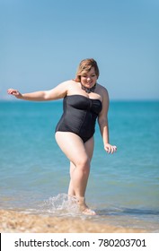 Overweight woman in black one-piece swimsuit at the sea. Fat girl comes from sea looking down and smiling