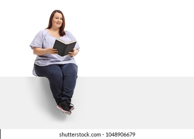 Overweight woman with a book sitting on a panel and looking at the camera isolated on white background