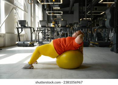 Overweight woman doing crunches exercise on fitness ball at gym