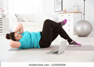 Overweight Woman Doing Exercise While Watching Tutorial On Laptop At Home