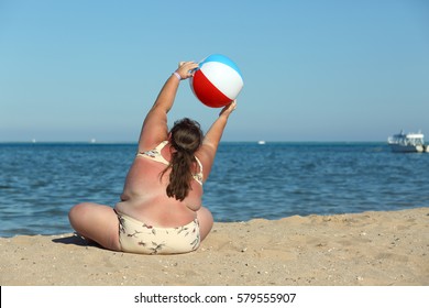 overweight woman doing gymnastics with ball on beach
