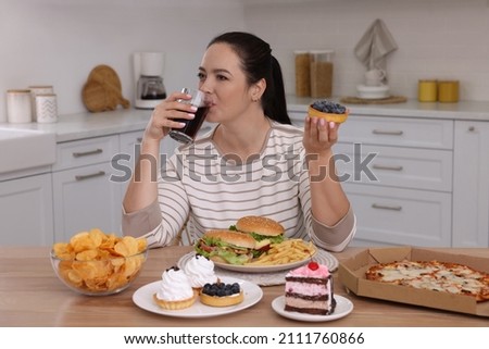 Overweight woman drinking cola and holding cake in kitchen. Unhealthy food 商業照片 © 