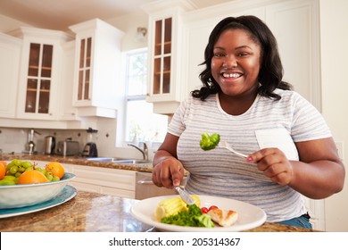 Overweight Woman Eating Healthy Meal In Kitchen