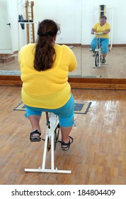 Overweight Woman Exercising On Bike Simulator From Behind