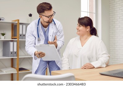 Overweight woman having consultation at doctor's office. Portrait of smiling doctor holding report file with appointment and giving consultation to a fat patient during medical examination in clinic. - Powered by Shutterstock