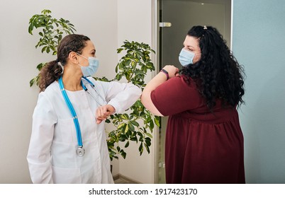 Overweight woman and her doctor wearing medical masks greeting each other by elbow bumping at doctor's office. Elbow bump, battle coronavirus epidemic