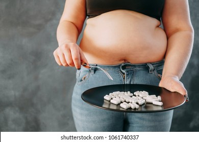 Overweight woman holding plate with slimming pills. Unhealthy way to get slim. Weight losing, dieting, fat burning, pharmacy, medicine concept