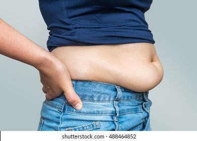 Overweight woman in jeans and fat on hips and belly isolated on gray background