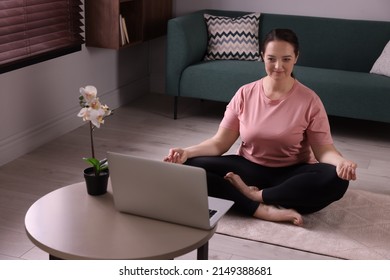 Overweight Woman Meditating On Rug While Watching Online Class At Home