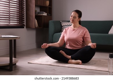 Overweight Woman Meditating On Rug While Watching Online Class At Home