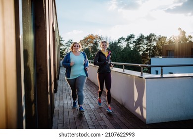 Overweight Woman Running And Exercising With Personal Trainer Outdoors On Gym Terrace.