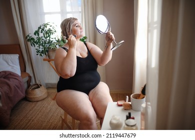 Overweight Woman Sitting And Looking At Mirror And Applying Make Up At Home, Selfcare Concept.