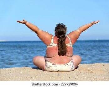 overweight woman sitting on beach with hands up 
