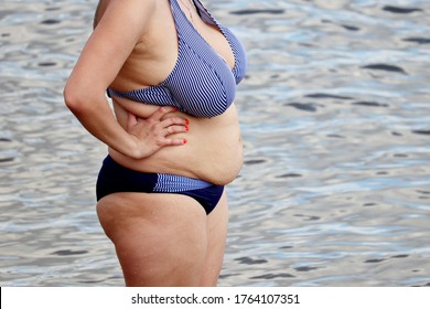 Overweight woman in swimsuit with fat belly standing in a water. Vacation on sea beach, overeating and weight loss concept