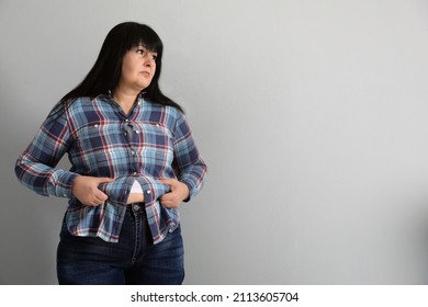 Overweight woman in tight shirt on light grey background. Space for text