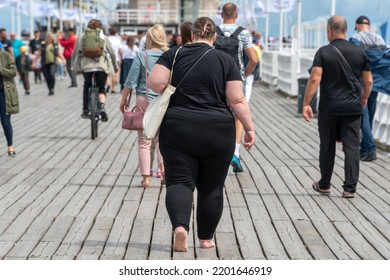 Overweight woman walking on the pier among people with normal weight. Barefoot obese woman wearing black. Obesity, losing weight. - Shutterstock ID 2201646919