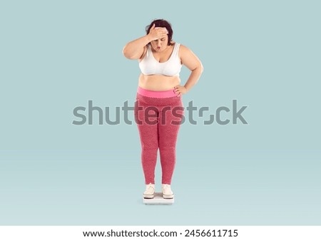 Overweight woman weighs herself. Big fat chubby plump obese lady isolated over light blue background stands on scales, looks at number, sees how many kilos she has gained and makes whistle of surprise