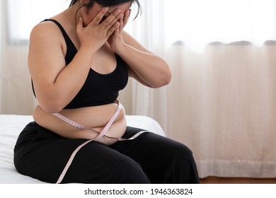 Overweight Women stressing over fat belly, using measuring tape. Overweight Woman Measuring Waist. Fat woman with tape measure, she uses her hand to squeeze the excess fat, surprise obese female. 