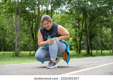 Overweight young woman with knee pain grabs her knee with both hands while sitting down at a running track of a local park - Powered by Shutterstock