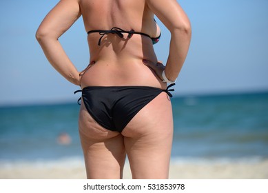 Overweight young woman in swimsuit near the sea, looking at the water, enjoys the hot sun in his summer holiday
