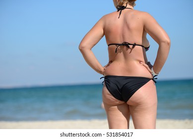 Overweight young woman in swimsuit near the sea, looking at the water, enjoys the hot sun in his summer holiday