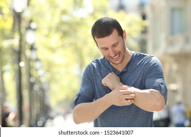 Overwhelmed adult man scratching itchy arm standing in the street