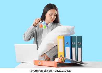 Overwhelmed Asian mother in suit with baby, laptop and office folders on blue background. Multitasking concept