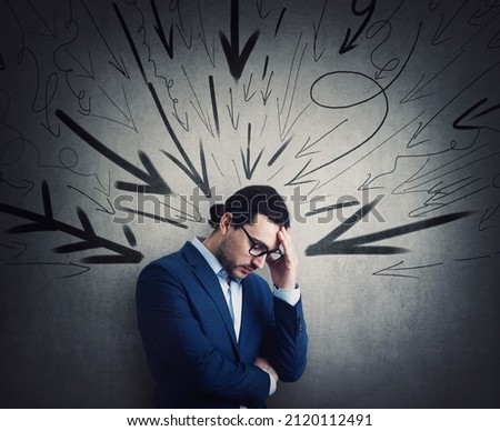 Overwhelmed businessman under pressure suffers headache and anxiety. High tension, dismay concept. Fatigue business person and multiple arrows points negativity towards him