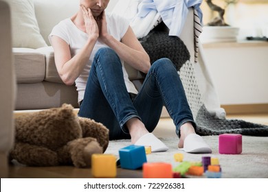 Overwhelmed Exhausted Woman Feeling Tired Of Cleaning In Her Messy House Sitting On The Floor With Toys And Laundry Lying Around Her