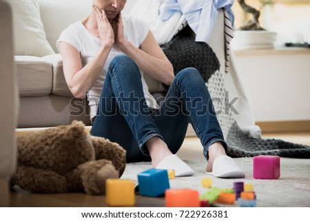 Overwhelmed exhausted woman feeling tired of cleaning in her messy house sitting on the floor with toys and laundry lying around her
