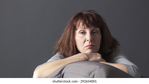 Overwhelmed Mature Woman Resting Her Face And Hands Laying Down On Cushions For Comfort While Being Sick Or Depressed