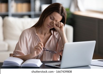 Overwhelmed unhappy young woman taking off glasses, rubbing eyes, feeling exhausted, working remotely on computer at home. Tired stressed lady suffering from dry eyes syndrome, massaging nose bridge.