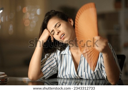 Overwhelmed woman suffering heat stroke fanning at home in the night