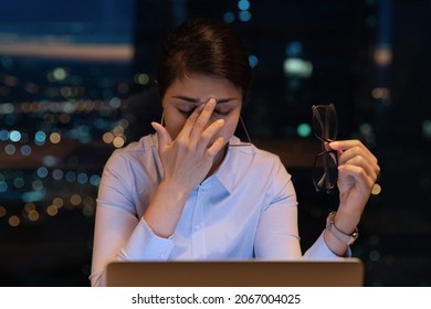 Overwhelmed Young Indian Businesswoman Taking Off Eyeglasses, Suffering From Blurry Eyesight, Massaging Nose Bridge Relieving Pain, Feeling Exhausted Working Late In Evening On Computer In Office.