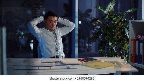 Overwhelmed Young Tired Asian Businessman Standing From Desk Leaving His Corporate Office Cabinet Late At Night. Concept For Workaholic, Exhaustion.