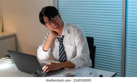 Overwork Concept The Office Personnel In The Loose Tie Sitting At His Desk, Reading A Paperwork And Typing On The Notebook.
