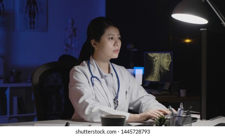 Overwork Deadline And People Concept. Doctor Woman With Computer And Coffee Working Late At Night In Dark Clinic Office. Young Nurse In White Lab Coat Typing On Patient Document In Midnight Hospital.