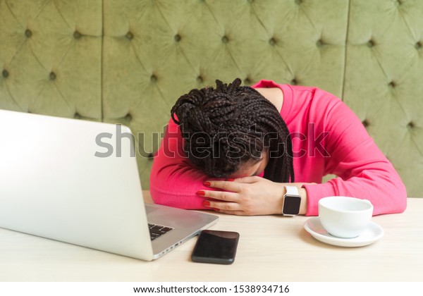 overwork and sleeping. Portrait of tired kind\
beautiful young freelancer with black dreadlocks in pink blouse is\
sitting in cafe and fall asleep on the table after too long\
working. Indoor