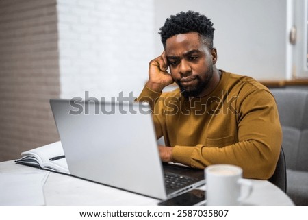 Overworked and anxious  freelancer using laptop while working remotely at his home office.