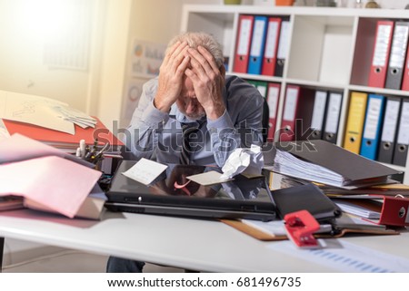 Overworked businessman sitting at a messy desk in office, light effect
