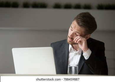 Overworked businessman in suit tired from laptop work, exhausted man feeling lack of sleep, headache or eye strain at workplace, office worker suffering from chronic fatigue after long using computer
