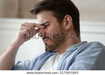 Overworked at computer. Tired exhausted millennial male employee businessman freelancer frowning rubbing bridge of nose suffering of eye pain dizziness blurry vision sudden headache or migraine attack