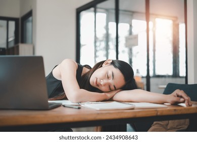 An overworked creative finds solace in a power nap at her work desk, surrounded by the tools of her trade, a temporary escape from the demands of a busy workday. - Powered by Shutterstock