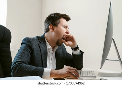 An overworked employee works on a desktop computer. Tired businessman or office worker yawns and falls asleep at the workplace. Sales manager, financial analyst or IT specialist, freelancer. - Powered by Shutterstock