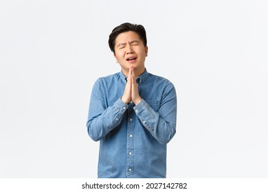 Overworked Gloomy And Sad Asian Man Begging For Help, Holding Hands Together Over Chest In Praying Gesture, Asking Favour, Showing Remorse, Standing White Background Overwhelmed