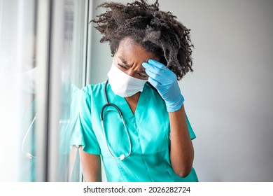 Overworked Healthcare Worker Holding Her Head In Pain At The Hospital During COVID-19 Epidemic. Nurse Having Headache And Tired From Work While Wearing PPE Suit For Protect Coronavirus Disease.