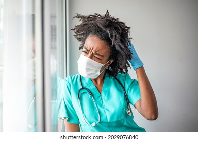 Overworked Healthcare Worker Holding Her Head In Pain At The Hospital During COVID-19 Epidemic. Nurse Having Headache And Tired From Work While Wearing PPE Suit For Protect Coronavirus Disease.