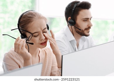 Overworked hotline operator in front of computer monitor and her busy coworkers at call centre office