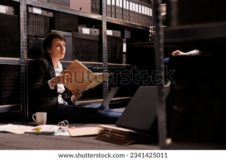 Overworked investigator sitting on floor in arhive room, analyzing crime scene documents. Criminology department private detectives working overhours at criminal case, checking victim report Foto stock © 