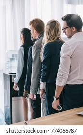 Overworked Managers Standing In Queue For Water Dispenser At Office